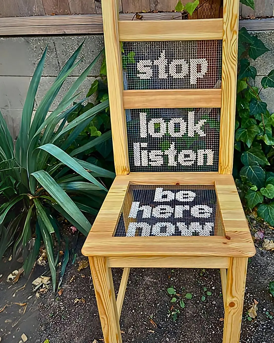 a wooden chair with the words 'stop, look, listen, be here now.' stitched on to wire mesh in the seat and back of the chair.