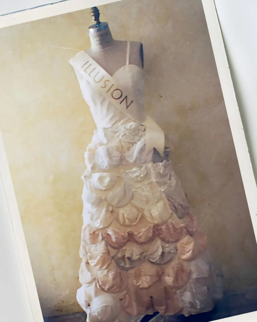 a mannequin wearing a dress made out of bras and a sash with the word ILLUSION written on it.