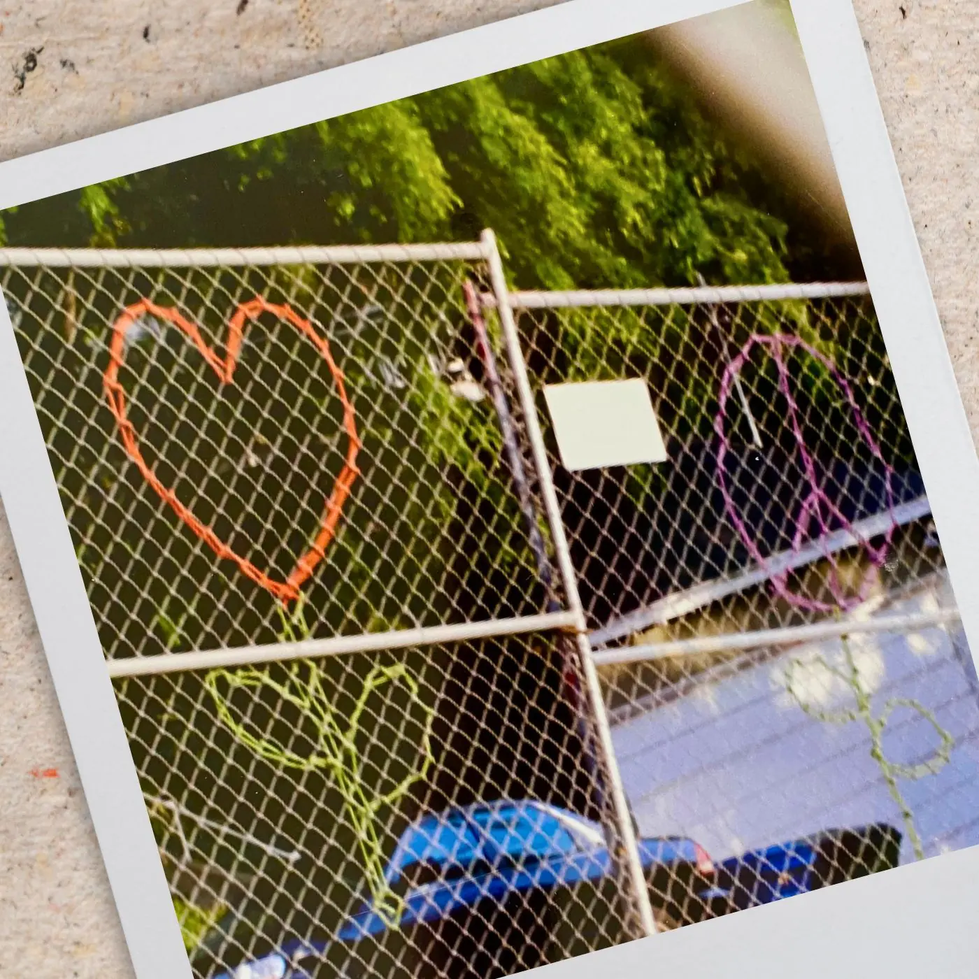 A heart shaped flower and a peace sign flower embroidered on to a fence with heavy yarn.