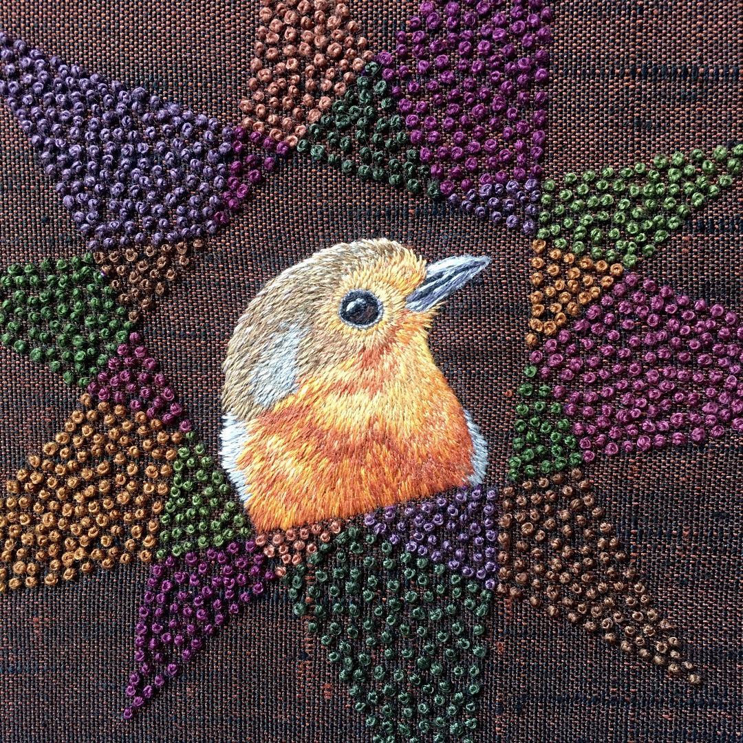 An embroidery of a robin on an embellished fabric background