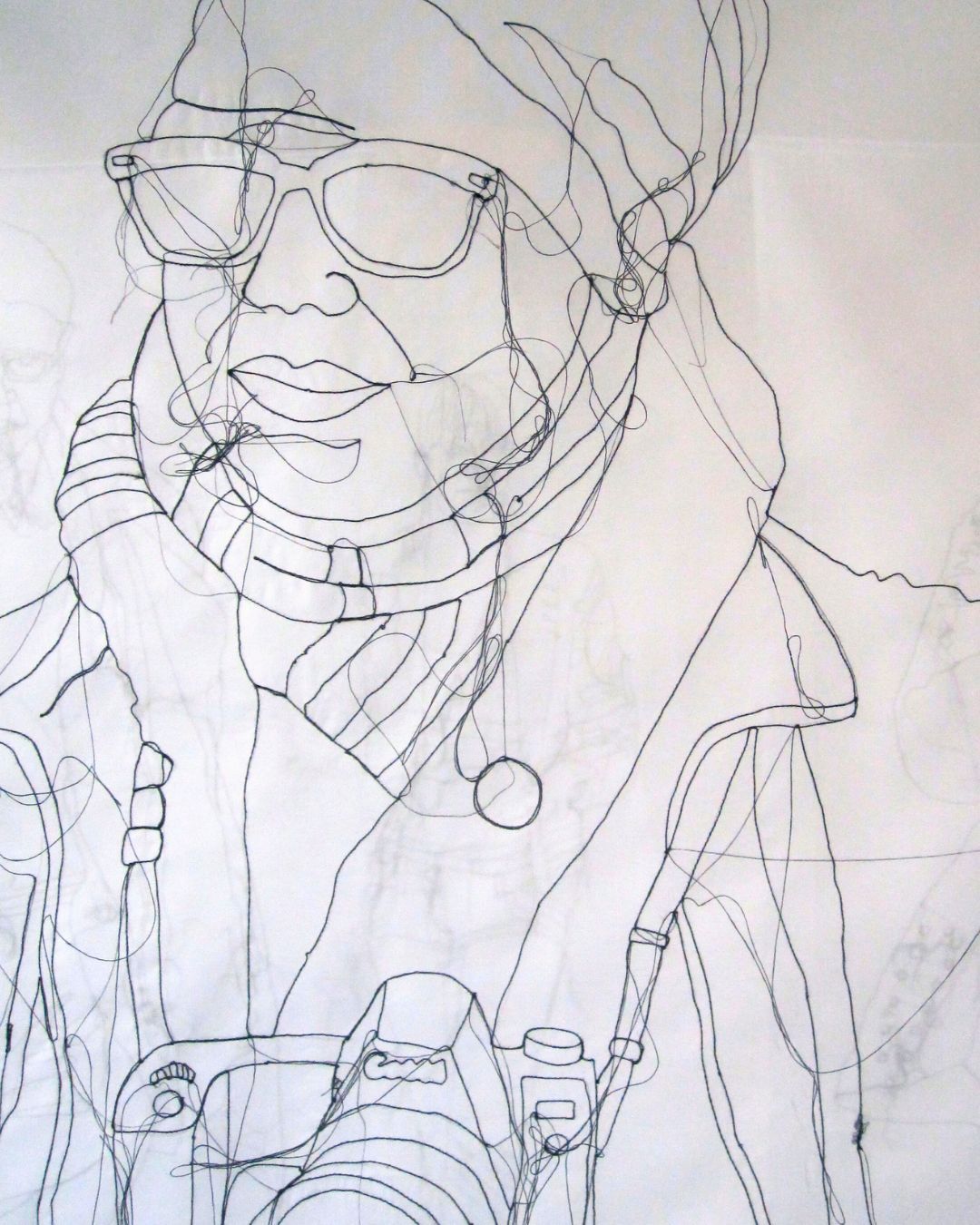 Close-up of stitched illustration of a winter-clad figure with sunglasses and camera, set on a semi-transparent background