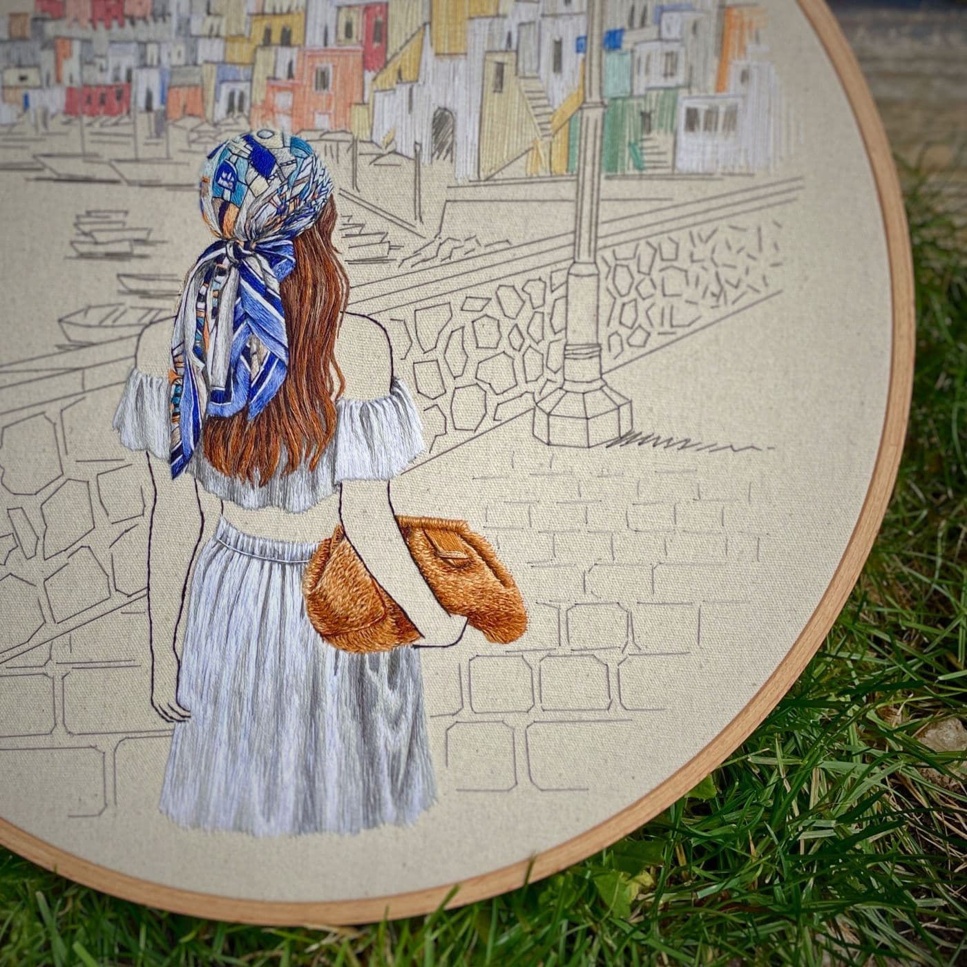 An embroidery on a hoop of a woman walking by the coast, in Italy. 