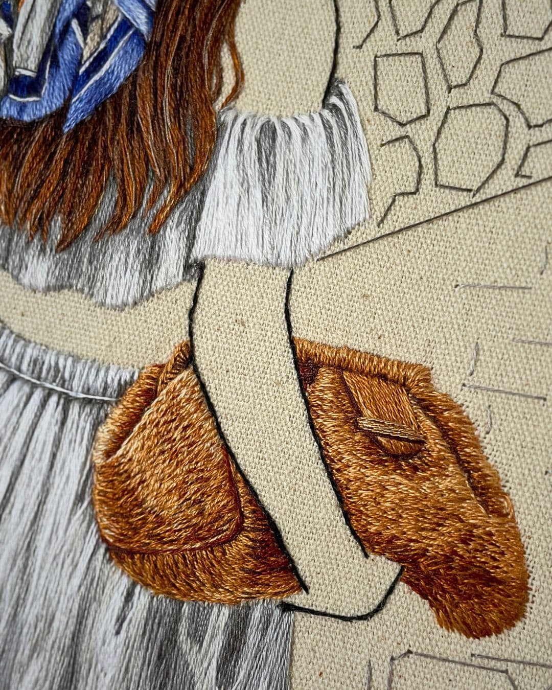 A close up of an embroidered artwork of a woman carrying a brown bag. 