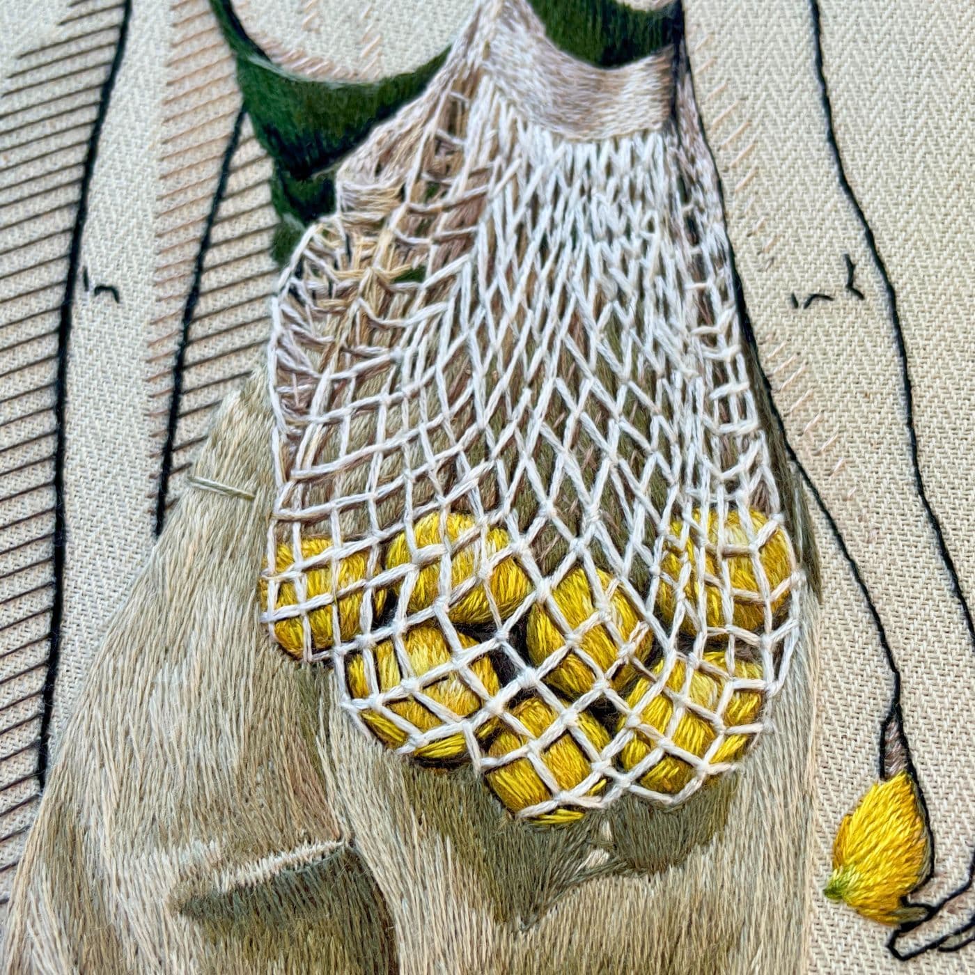 A close up of an embroidered artwork of net bag filled with lemons