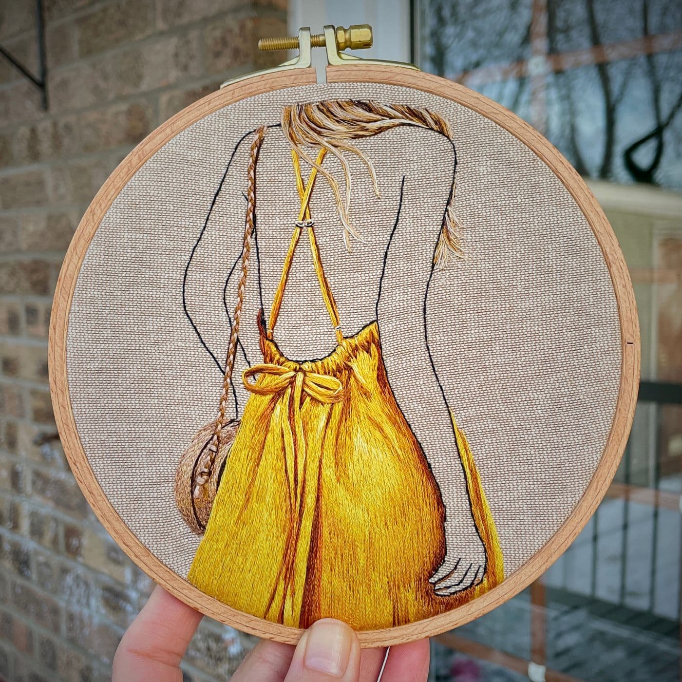 An embroidery hoop with a stitched artwork of a woman wearing a bright yellow outfit.