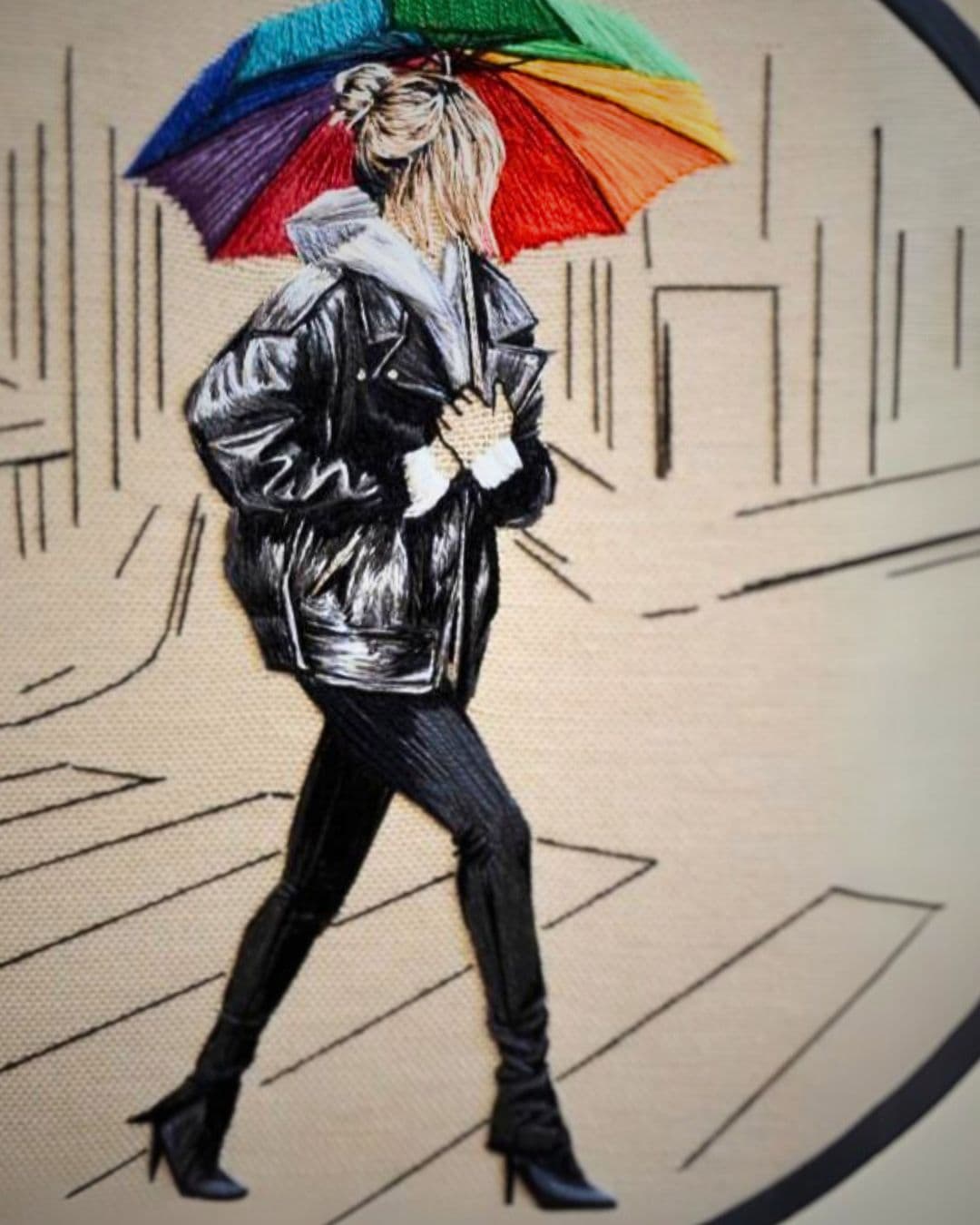 A stitched artwork of a girl with a multicoloured umbrella. 