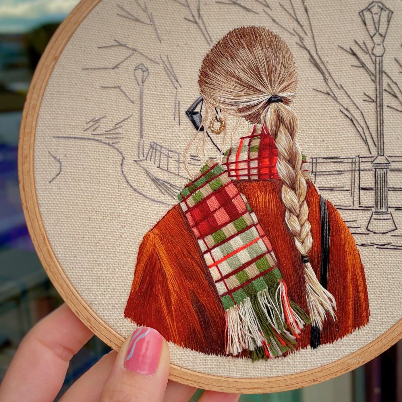 An embroidery hoop with a stitched artwork of a girl with tartan scarf. 