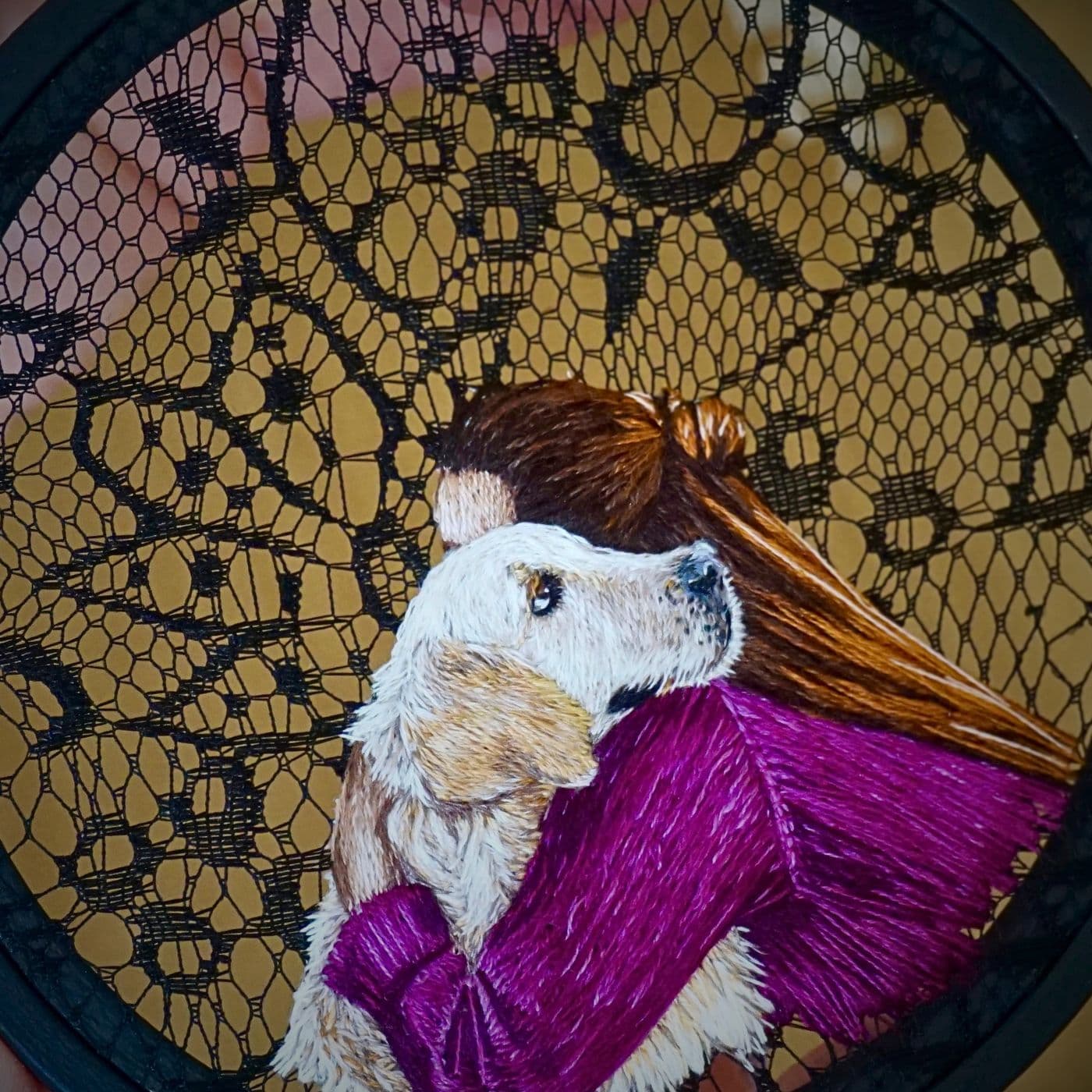 An embroidery on a blcak lace hoop of a woman hugging a golden retriever dog. 