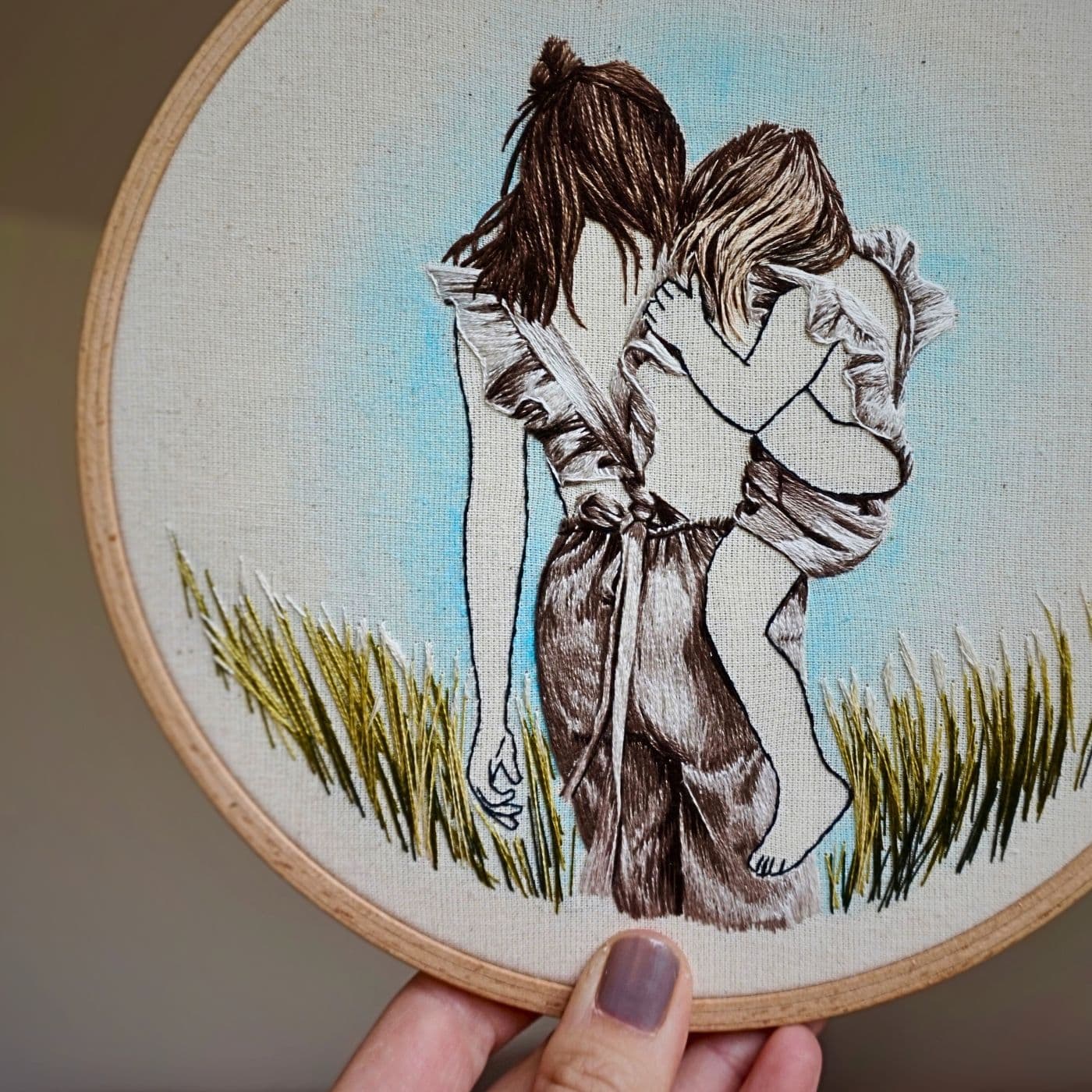 An embroidery hoop with a stitched artwork of a mother holding her child on her hip.