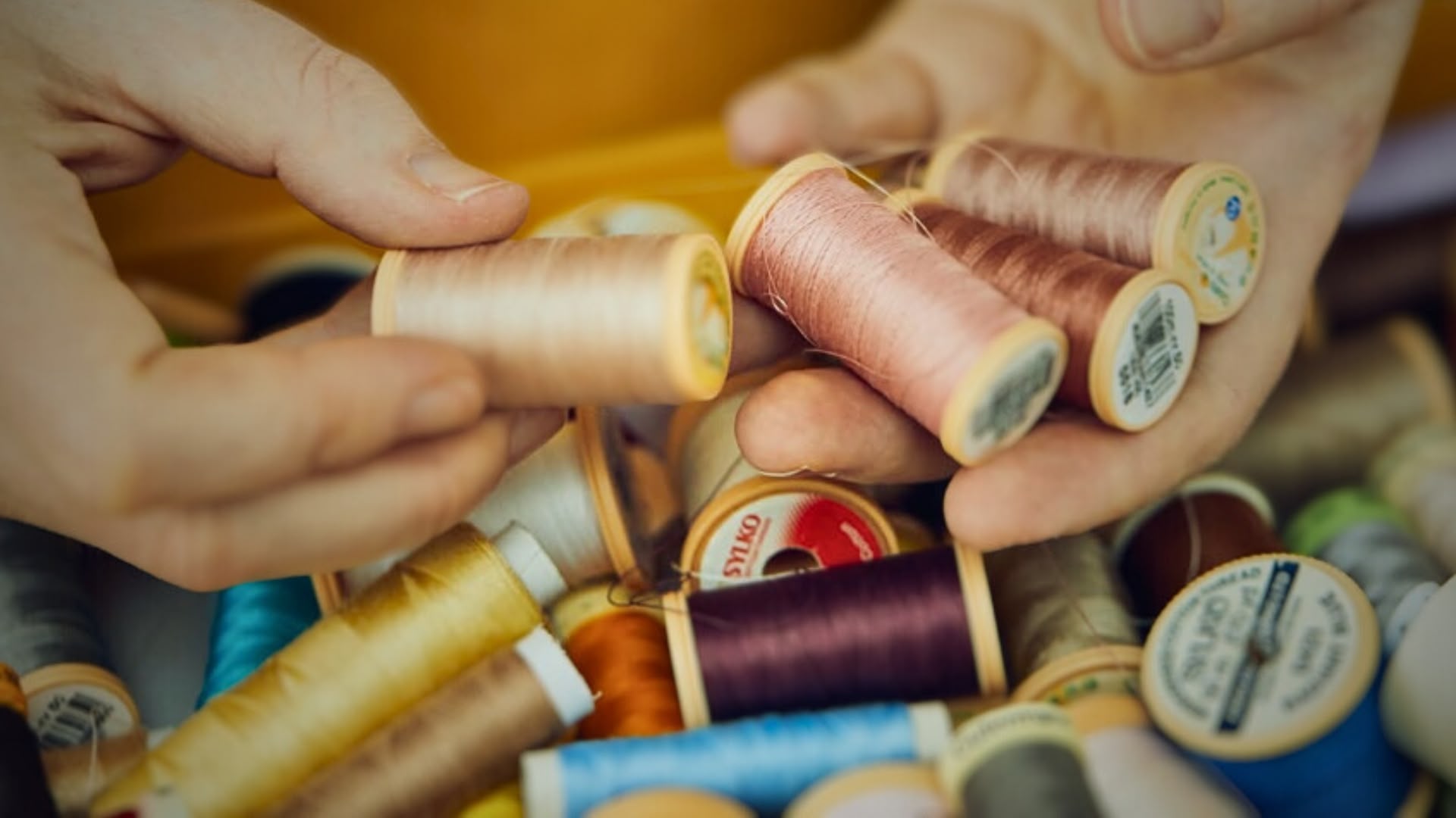 Hands picking out spools from a collection of threads