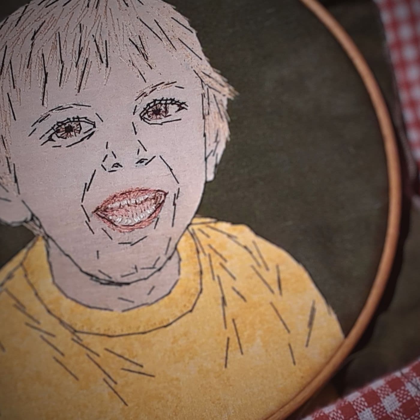 A stitched portrait of a young boy smiling, in an embroidery hoop