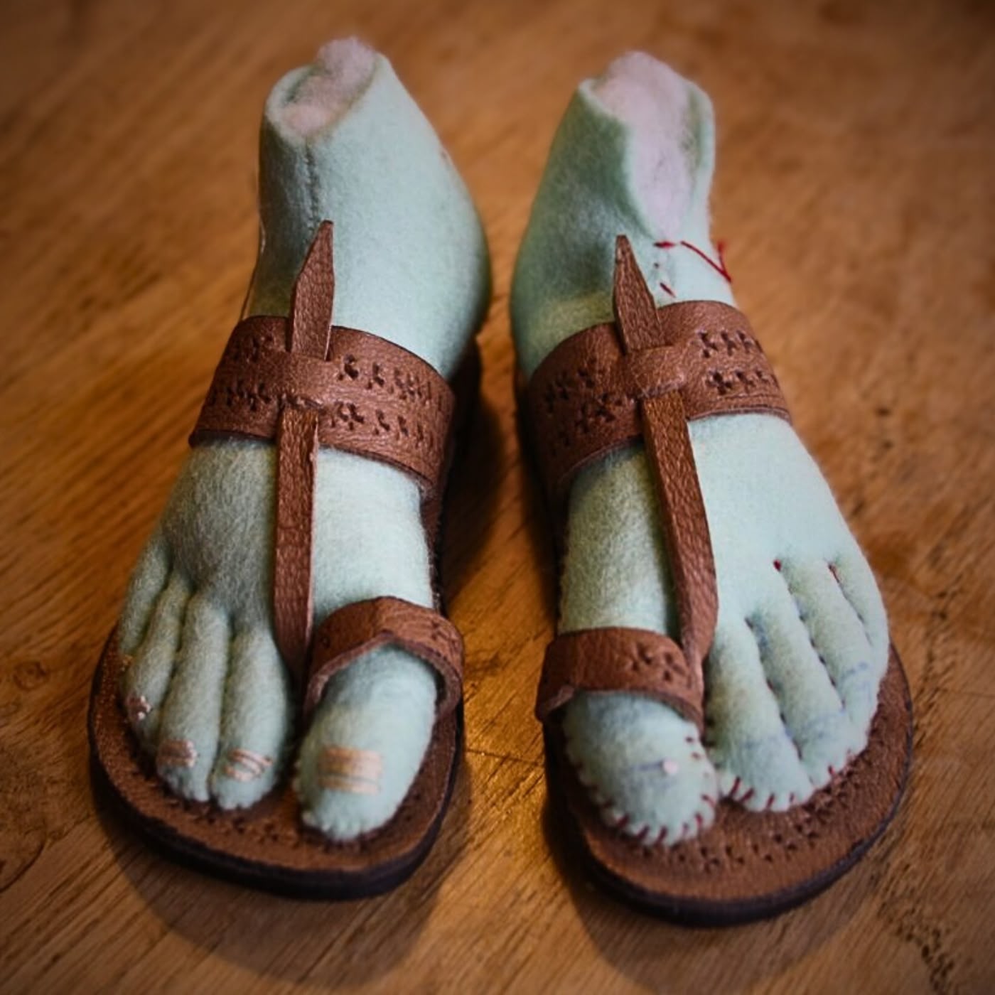 a pair of stuff doll's feet in sandles on a wood surface