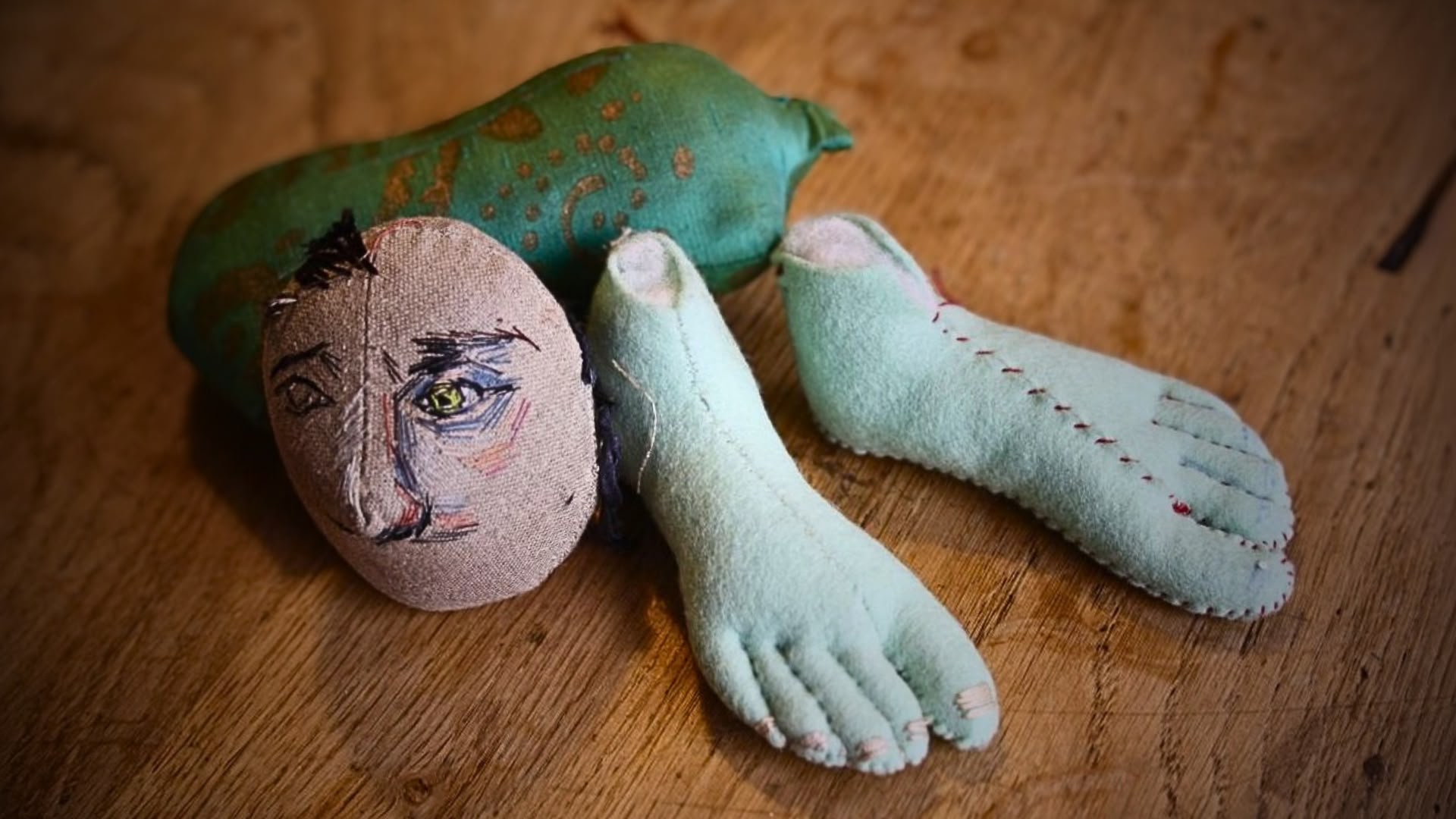 head and feet stuffed doll parts laid on a wood surface