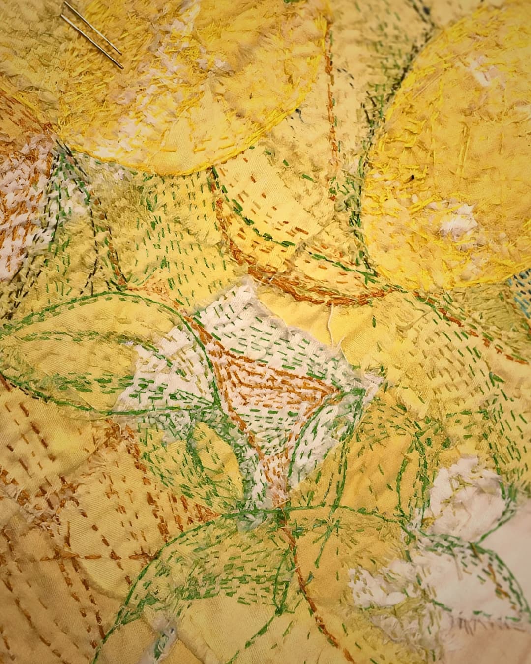 A yellow fabric collage with green and yellow decorative stitching