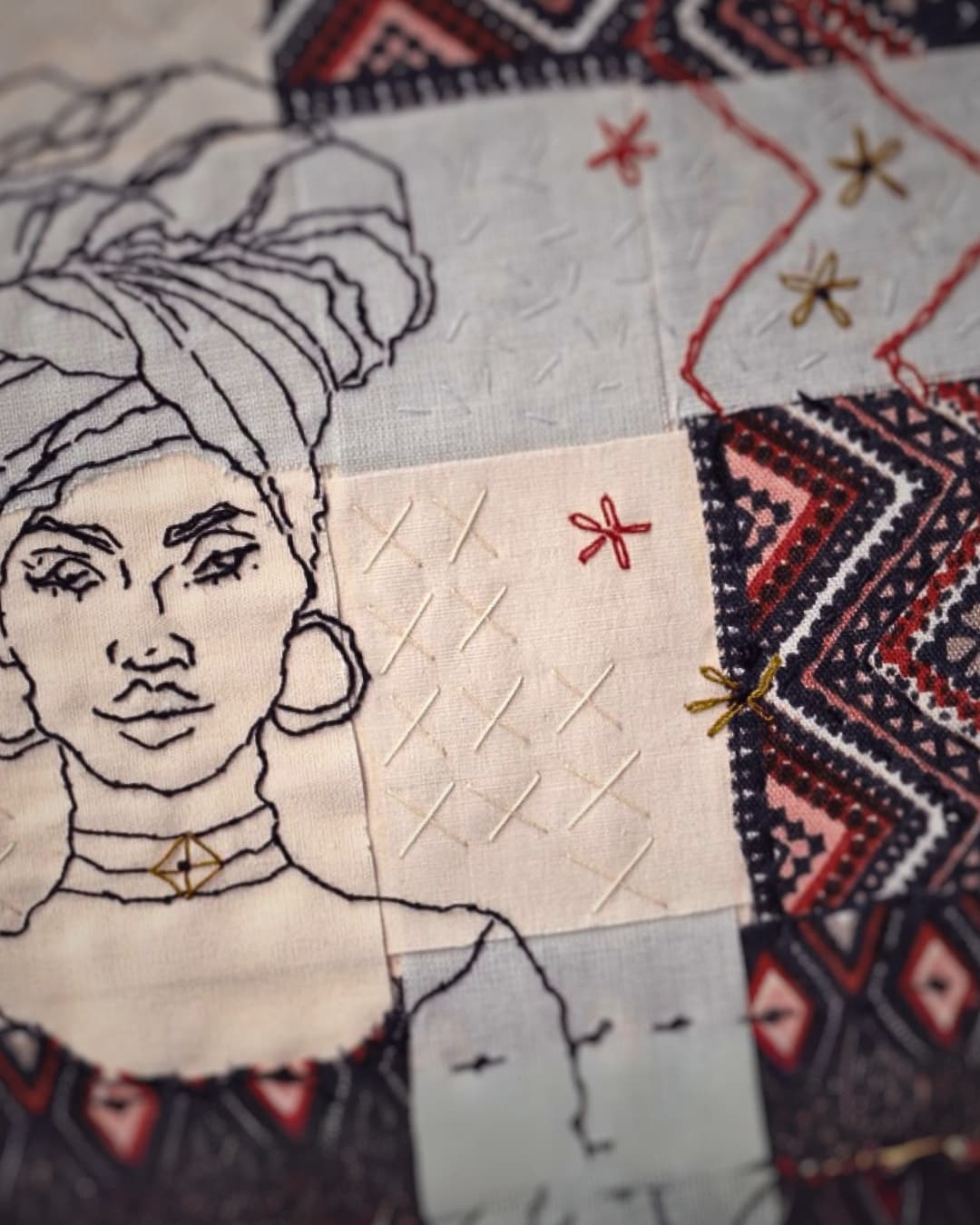 A close up of a simple hand stitched portrait of a lady wearing a head scarf surrounded by decorative stitches