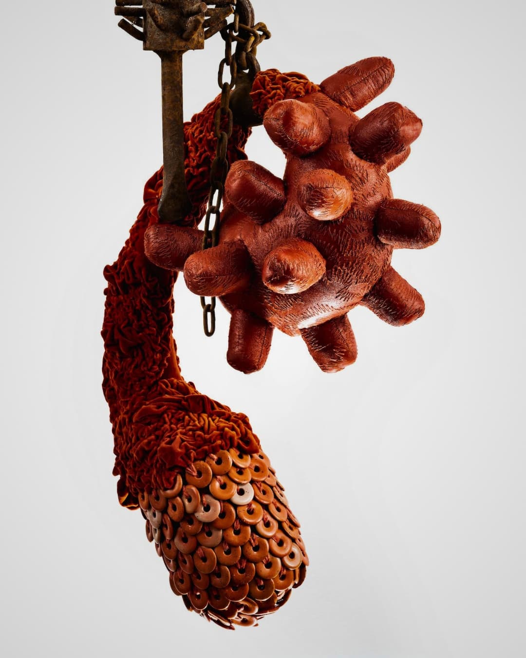 A red stitched scuplture of an abstract cell mutation hanging from a chain.