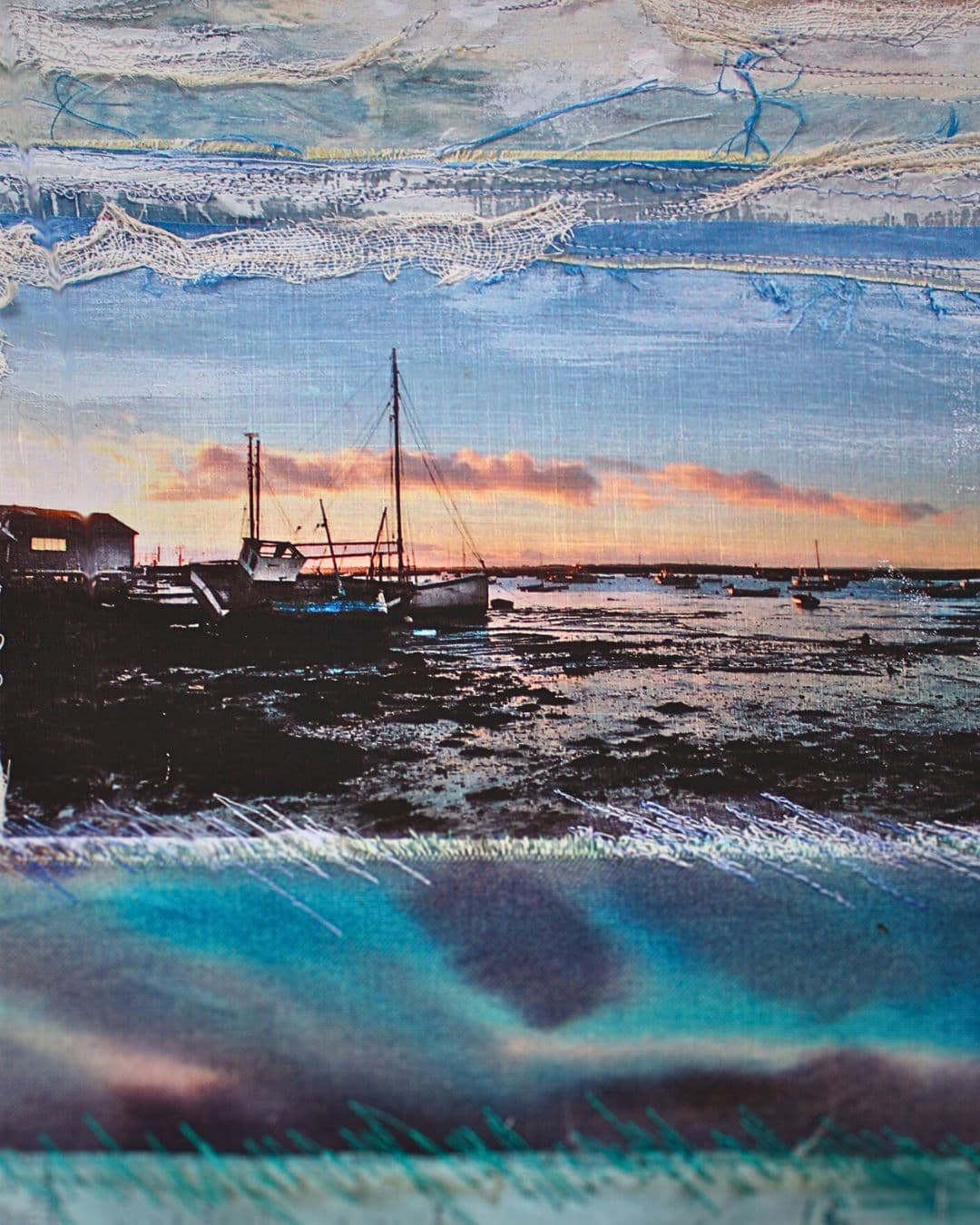 A stitched, fabric artwork of a boat on the water at sunset.