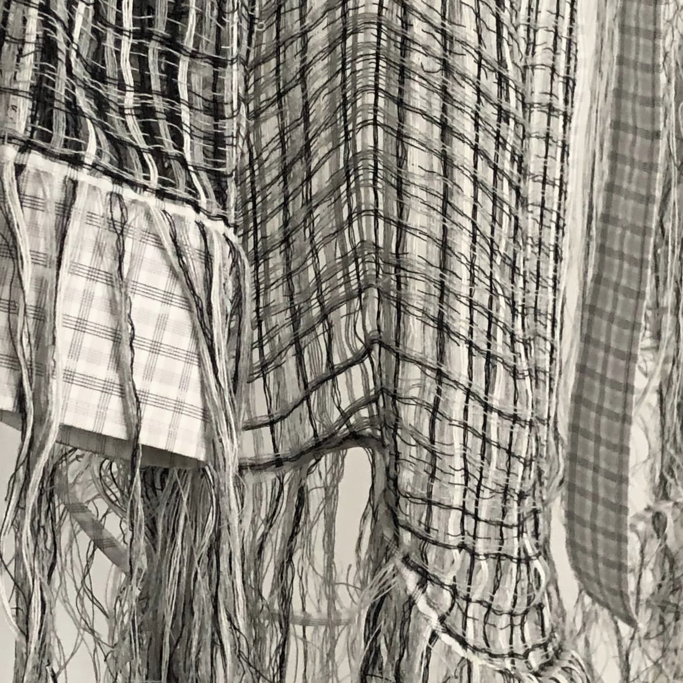 A close up of a mens shirt that has been shredded and rewoven with white and black loose hanging threads. 