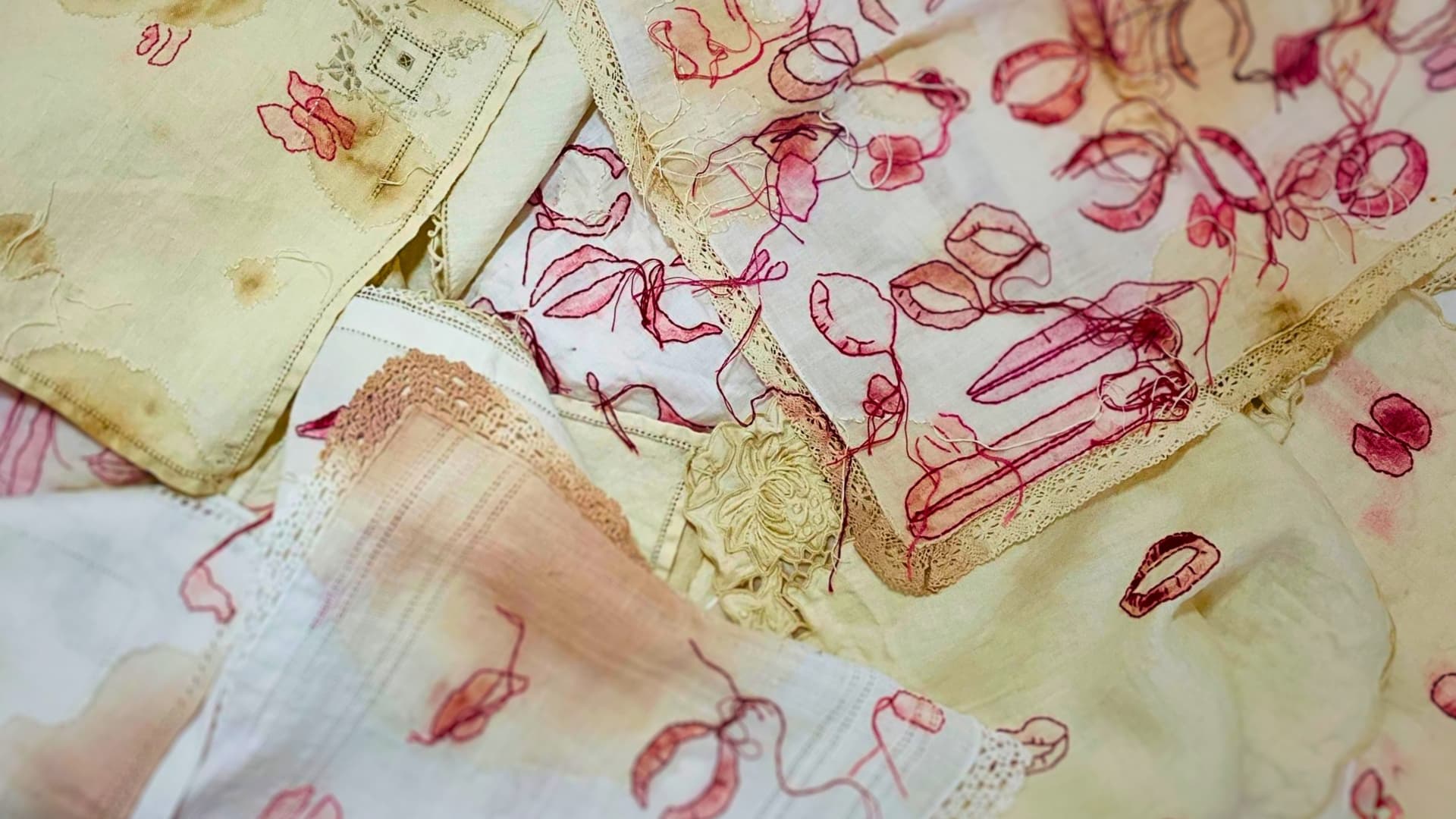 A pile of fabric handkerchiefs with red embroidered 'lipstick' stains