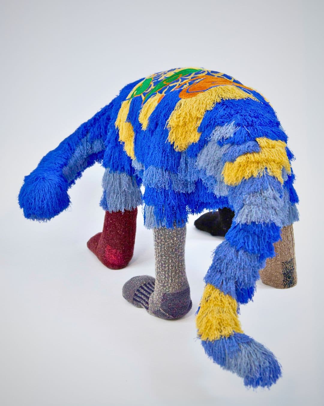 A stitched artwork of a Dinosaur embellished with colourful yarn and colourful socks!