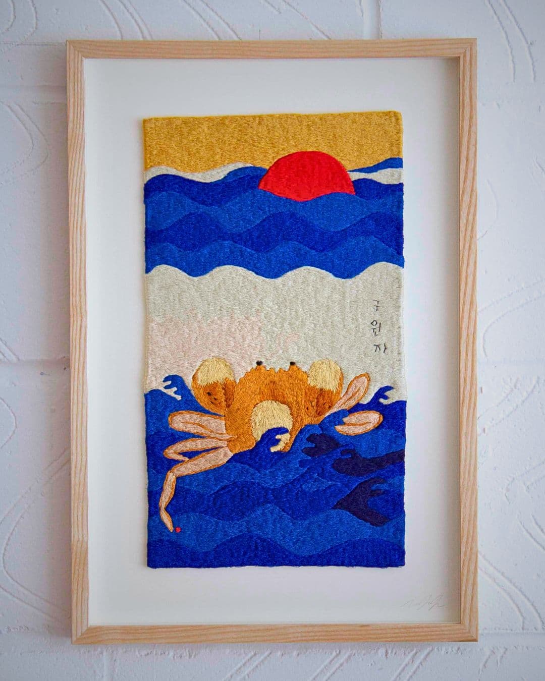 A framed textile artwork of a crab on a wall