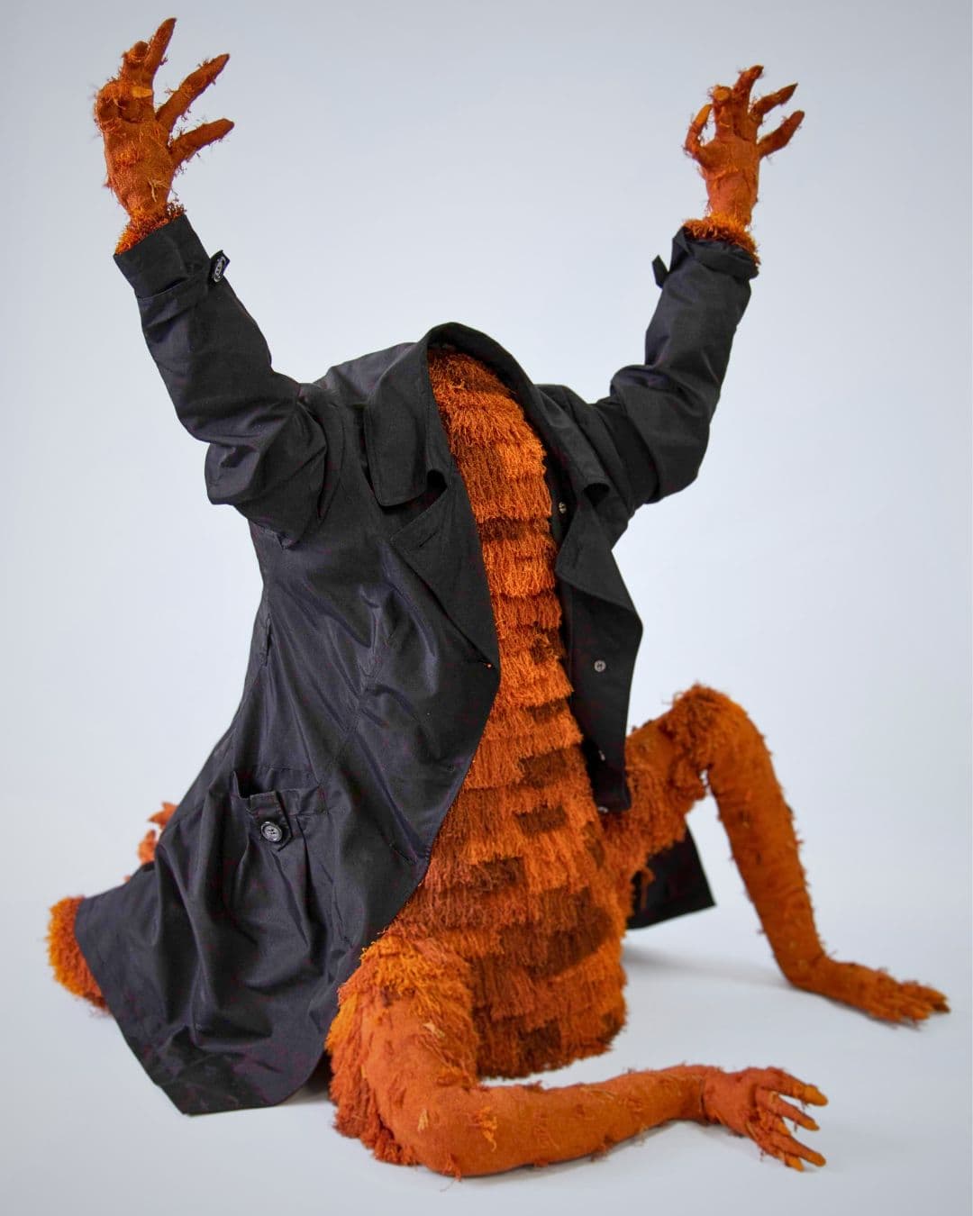 A stitched sculpture of a headless orange creature wearing a jacket.