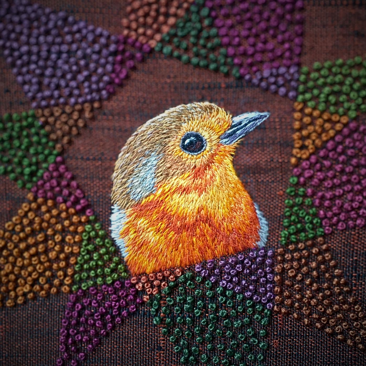 An embroidery of a robin on an embellished fabric background