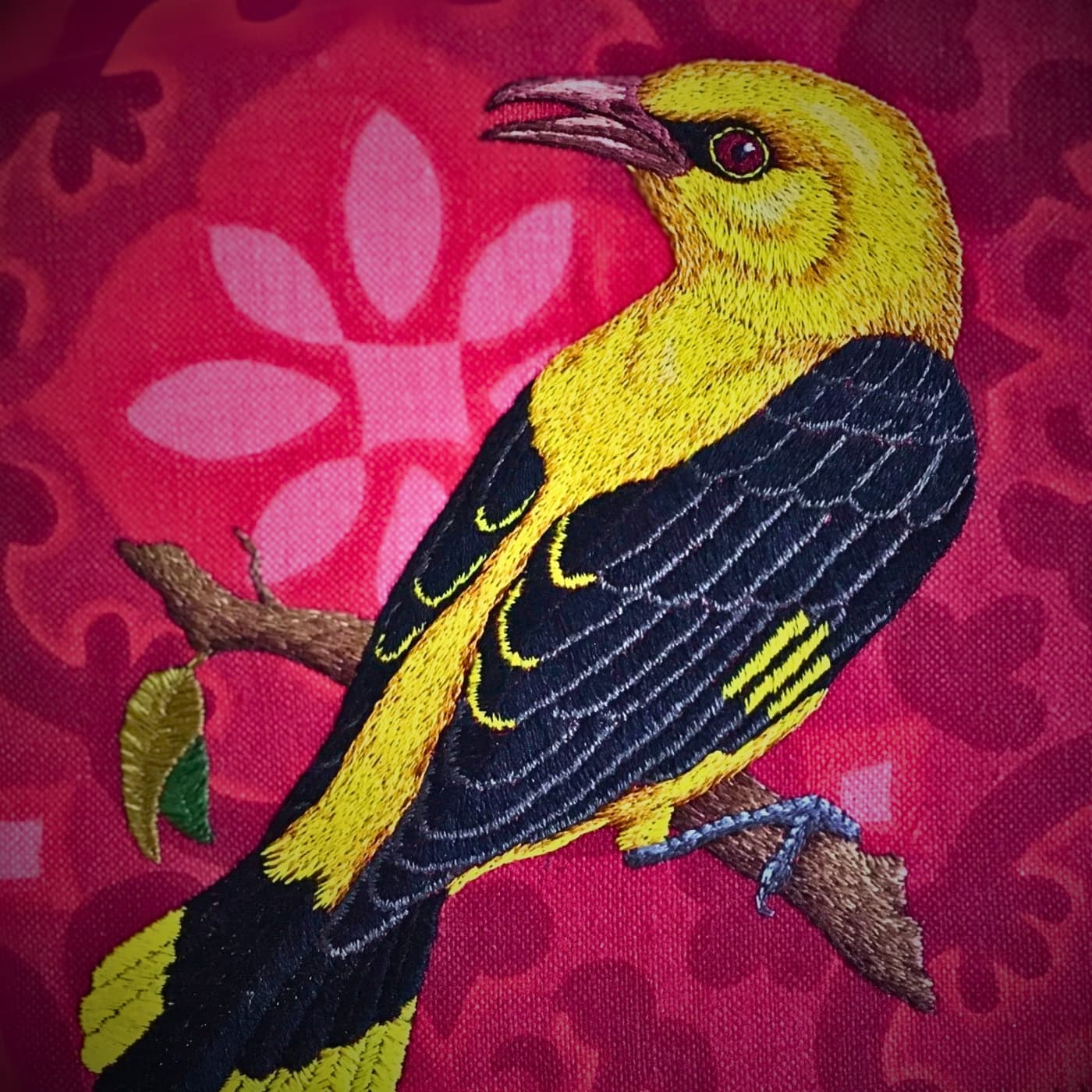 An embroidery of yellow bird on a pink patterned fabric.