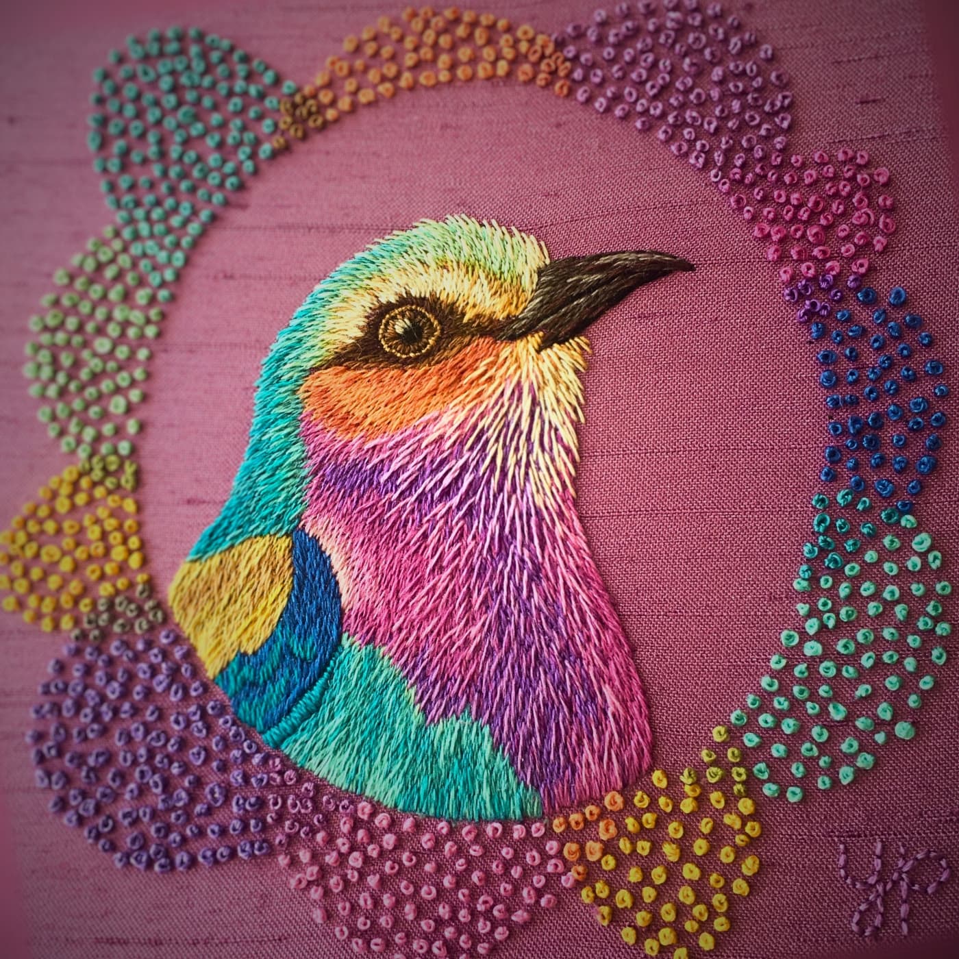 A colourful bird embroidery on a pink surface fabric background.