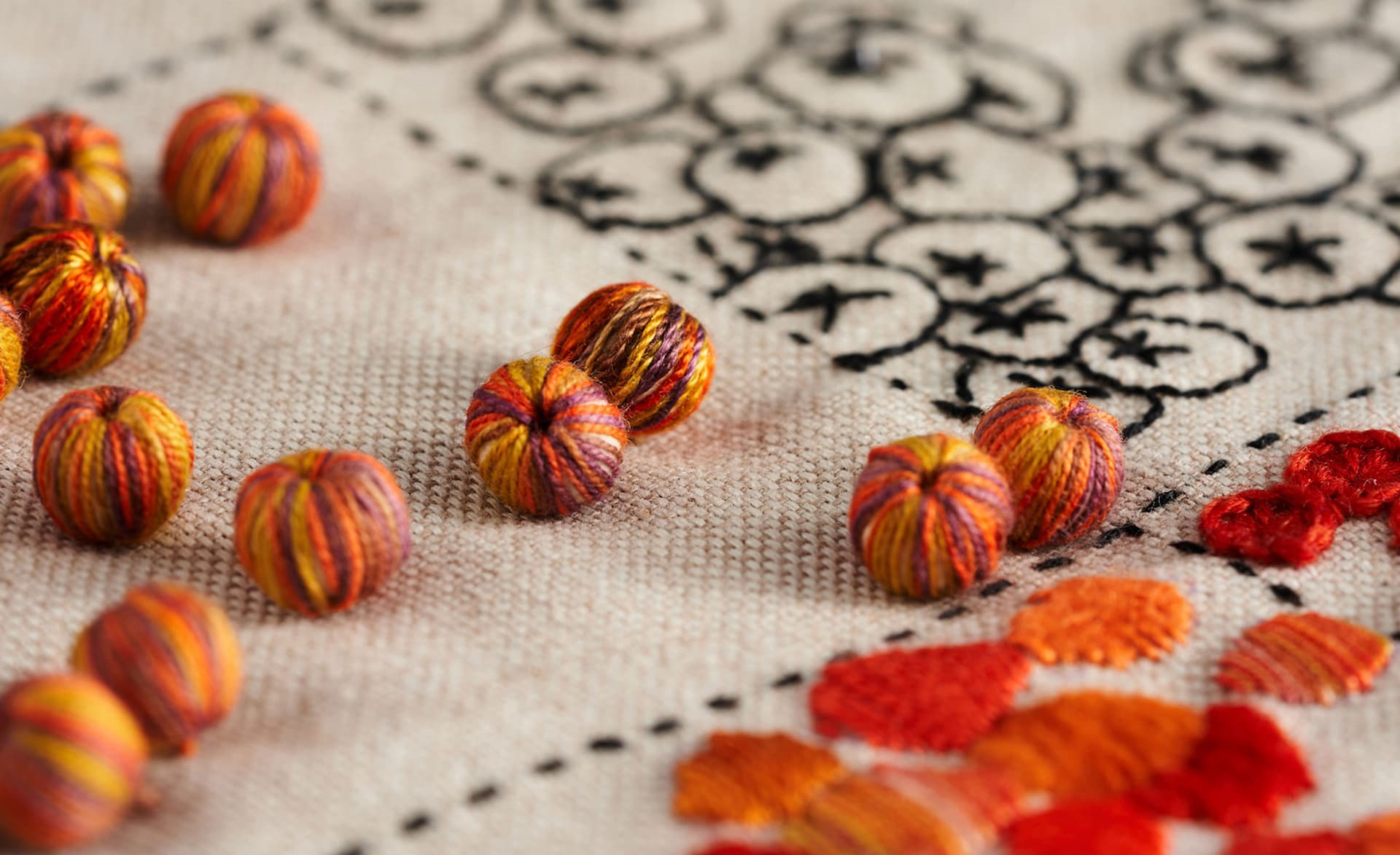 Close-up of vibrant, multicolored embroidered textile balls on a detailed embroidery pattern, showcasing intricate craftsmanship in textile art.