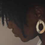 Profile of Nneka Jones, textile artist, in deep concentration as she works on her intricate art piece, wearing statement earrings